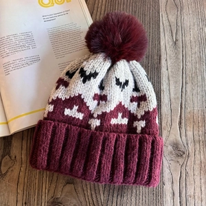 Macro view of knit beanie featuring thick striped texture and burgundy fluffy pom-pom