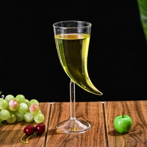Unique horn-shaped glass cocktail goblet on a stem with yellow drink against dark background