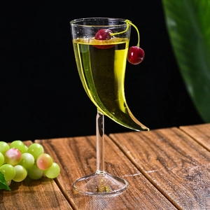 Unique horn-shaped glass cocktail martini glass with cherries on a wooden table