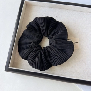 Dettaglio di uno scrunchie nero plissettato con texture morbida su un vassoio beige