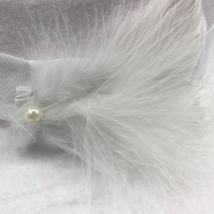 Detailansicht eines weißen Feder-Accessoires mit Schleife und Perle auf dem Wollhut
