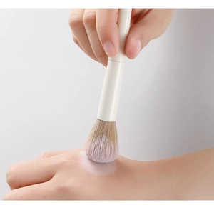 Close-up of soft synthetic bristles applying loose powder on hand with white handle