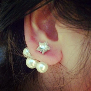 Close-up of star stud earrings with dangling white pearls behind the ear lobe