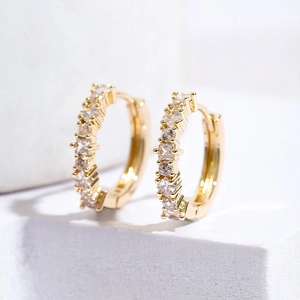 Close-up of gold hoop earrings with square blue zircon inlay on white minimalist background