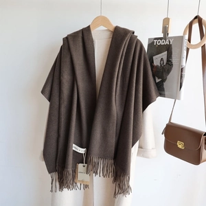 Detail of dark brown knit scarf with fringe hanging on white coat with fashion accessories