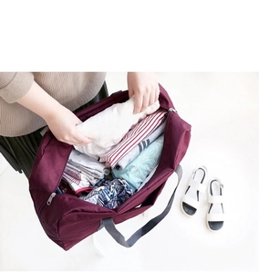 Macro view of burgundy travel organizer bag being packed with clothes on white background
