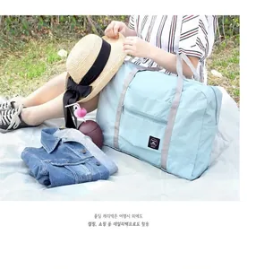 Foldable light blue travel bag with gray handles and logo on a green grass background