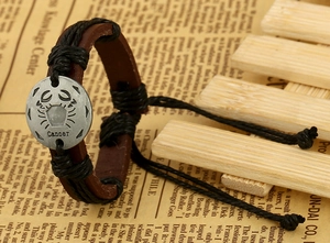 Macro shot of Cancer zodiac sign on a vintage braided leather bracelet with silver pendant