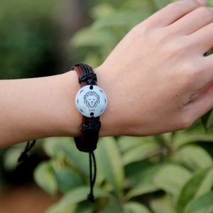 Adjustable brown leather braided bracelet featuring a white Leo zodiac charm on wrist
