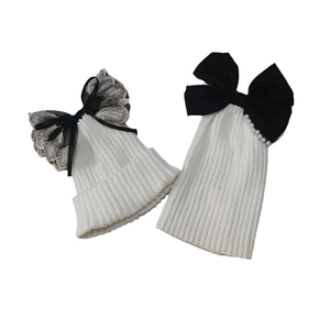White ribbed knit beanie hats for women with pearl lace bow accents on plain background
