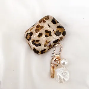 Coque AirPods léopard élégante avec porte-clé perle et coquillage sur tissu blanc