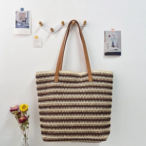 Brown and beige striped raffia straw tote bag with PU leather straps hanging on a wall