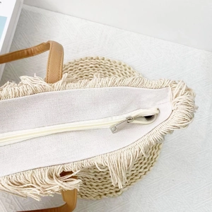 Close-up of beige woven tote bag with silver zipper closure and tassel fringe detail