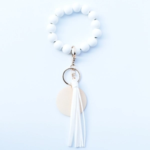 White beaded bracelet keychain with leather tassel and wood charm on blue background