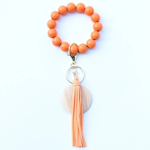 Detail of orange beaded keychain bracelet with wood charm and faux leather tassel