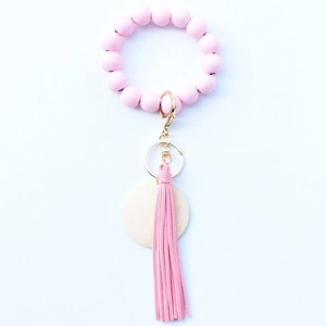 Pink wooden bead bracelet keychain with leather tassel and gold ring on white background