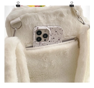 Macro shot of side zipper pocket on plush white faux fur bag with a phone inside