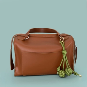 Brown leather handbag featuring a stylish green hand-woven braided tassel bag charm