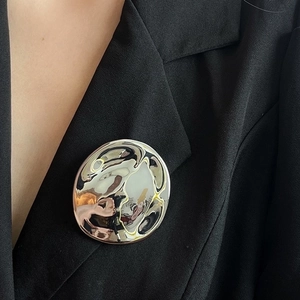 Minimalist irregular round metal brooch with silver wavy texture on black blazer