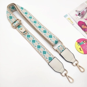 Macro view of adjustable woven shoulder strap with green geometric embroidery and gold clips