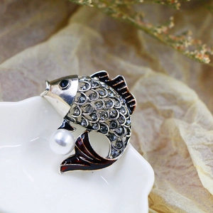 Detailed view of silver fish brooch with grey rhinestones, white pearl, and red enamel