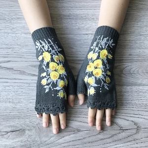 Grey fingerless knitted gloves with yellow flower embroidery on a wooden table