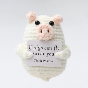 Close-up of handmade crochet pig doll holding motivational card with positive quote