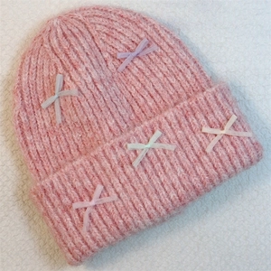 Close-up of pink knit beanie featuring delicate ribbon bows and thick ribbed texture