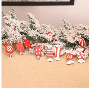 Detail of red and white wooden candy ornaments hanging on snowy pine branches