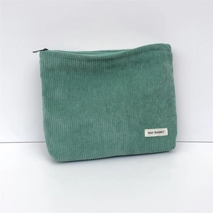 Detail of green corduroy makeup bag featuring soft ribbed texture and a branded fabric label
