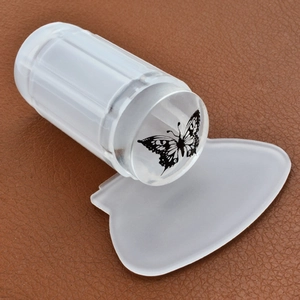 Clear silicone nail stamper with butterfly pattern and white scraper on brown leather surface