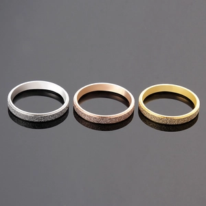 Three minimalist matte titanium steel rings in silver, rose gold, and gold on dark surface