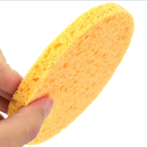 Hand holding a yellow round wood pulp sponge for facial cleansing and exfoliating