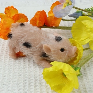 Realistic silicone piglet toy with pink skin and black spots on white waffle fabric