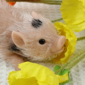 Close-up of a realistic silicone piglet toy with beige fur and black spots among flowers