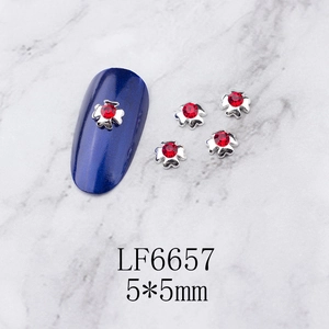 Macro detail of 5x5mm silver flower nail charms with red rhinestones on blue nails