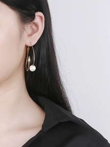 Detail of elegant gold curved hook earrings with large white pearls on a model