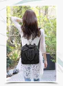Outdoor shot of a black faux leather backpack worn by a model on the back