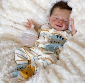 Close-up of 20 inch reborn baby doll in cat pajamas with a bottle on soft white blanket