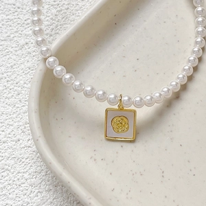 Gold plated copper necklace with square mother of pearl rose pendant on a ceramic tray