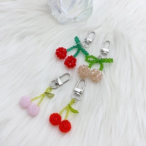 Cute beaded cherry keychains in red, pink and gold on soft white plush background