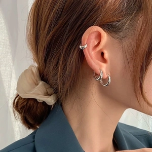 Close-up of polished silver hoop earrings and minimalist ear cuff on model ear