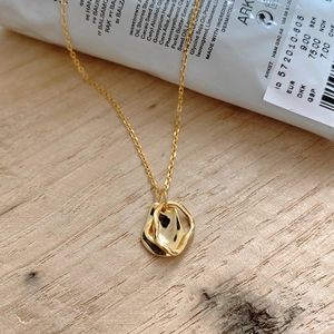 Detail of gold organic layered pendant on thin chain over minimalist wood background