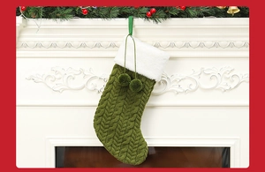Close-up of green knitted Christmas stocking with white pom-poms on a white fireplace