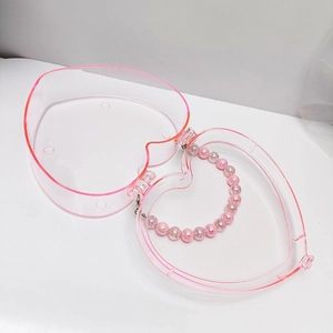 Draufsicht auf eine herzförmige transparente Box mit rosa Rand und Perlenketten-Inhalt