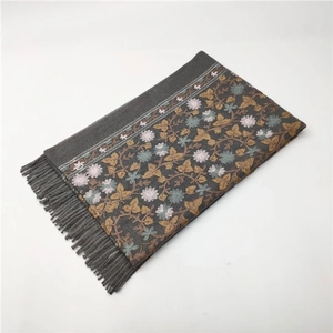 Close-up of thick scarf with floral embroidery and tassel fringe on grey cashmere-like fabric