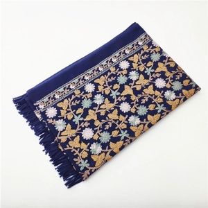 Close-up of deep blue cashmere scarf featuring golden and pink floral embroidery with tassels