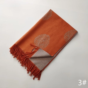 Detailed view of orange and beige double-sided knitted scarf with tree pattern and fringes