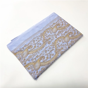 Detailed view of light blue cashmere-like shawl with golden paisley embroidery and tassels