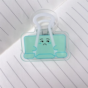Primo piano di una clip in acrilico verde chiaro con emoji triste su carta a righe